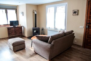 Una sala de estar con sofá, reposapiés, televisor, chimenea y una ventana con persianas.