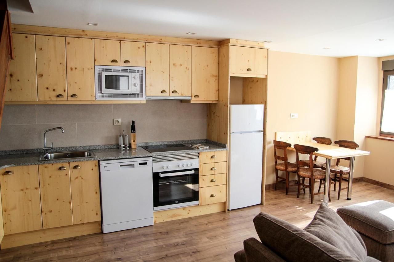 Cocina compacta con muebles de madera, microondas, estufa y refrigerador. Cuenta con una zona de comedor con mesa y sillas.