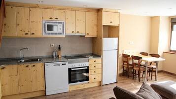 Cocina compacta con muebles de madera, microondas, estufa y refrigerador. Cuenta con una zona de comedor con mesa y sillas.
