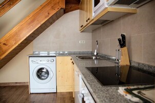 Pieni, käytännöllinen keittiö, jossa on pyykinpesukone, pesuallas ja puukehikoiset kaapit.
