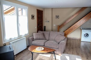 Sala de estar com sofá, mesa de centro, radiador, máquina de lavar e escada.