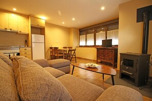 Sala de estar con un sofá, una mesa de centro y una chimenea. Hay una zona de cocina con armarios y un refrigerador.