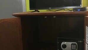 A television on a wooden stand with a remote control and a small electronic device below it. - Andreas Tulum Hotel (Tulum)