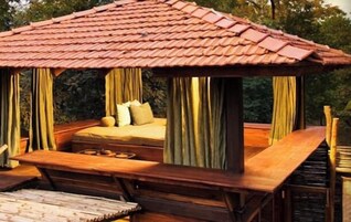 Un pabellón de madera con techo de tejas, una cama con almohadas y una mesa.