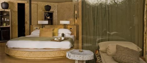 A bedroom with a large bed, bedside tables, a small sofa, and a view of trees through a window.