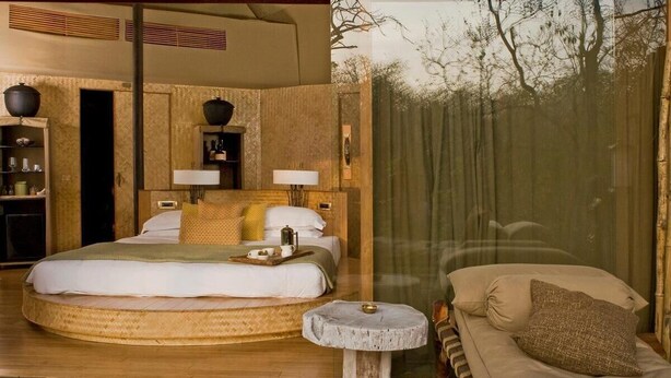 A room with a bed, bedside tables, a mirror, and a view of trees through a window. - Banjaar Tola, A Taj Safari (Bichhiya)