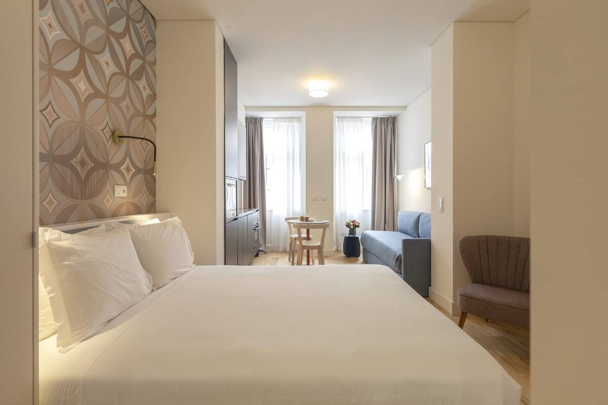 A hotel room with a large bed, a small table with chairs, a sofa, and a chair.