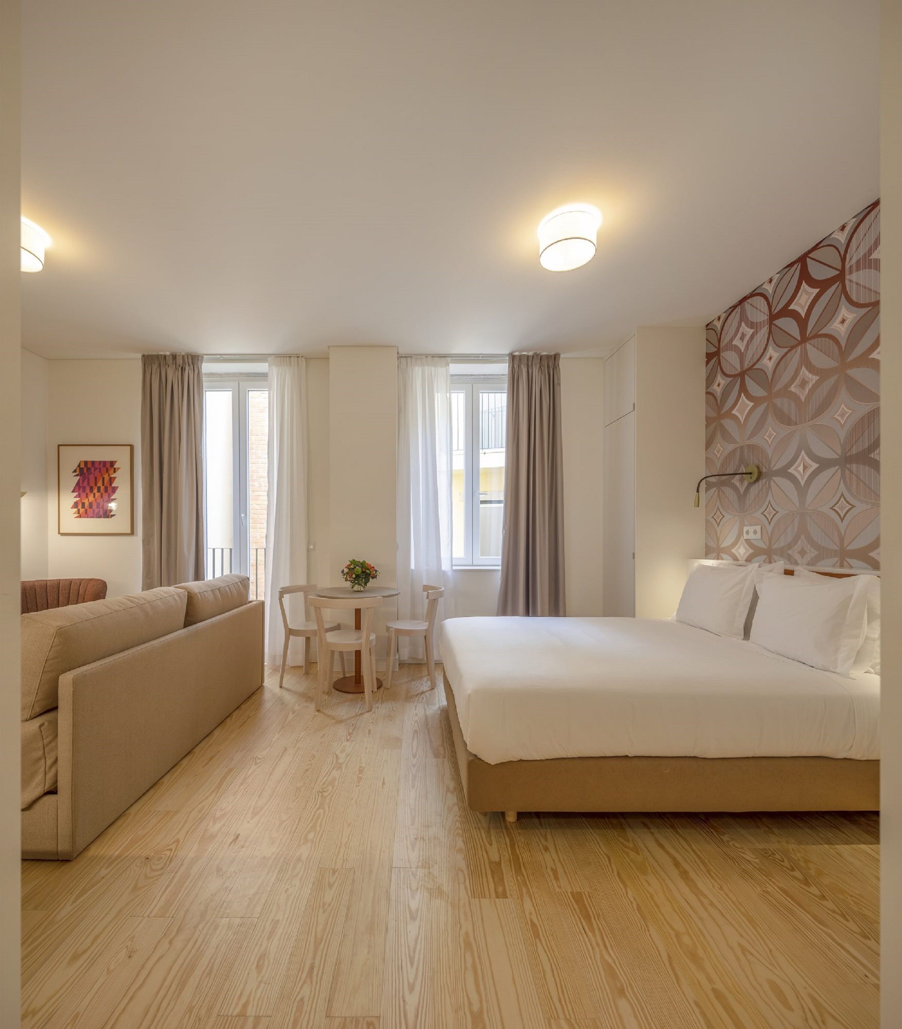 A hotel room with a bed, a sofa, a small table with chairs, and a window with curtains.