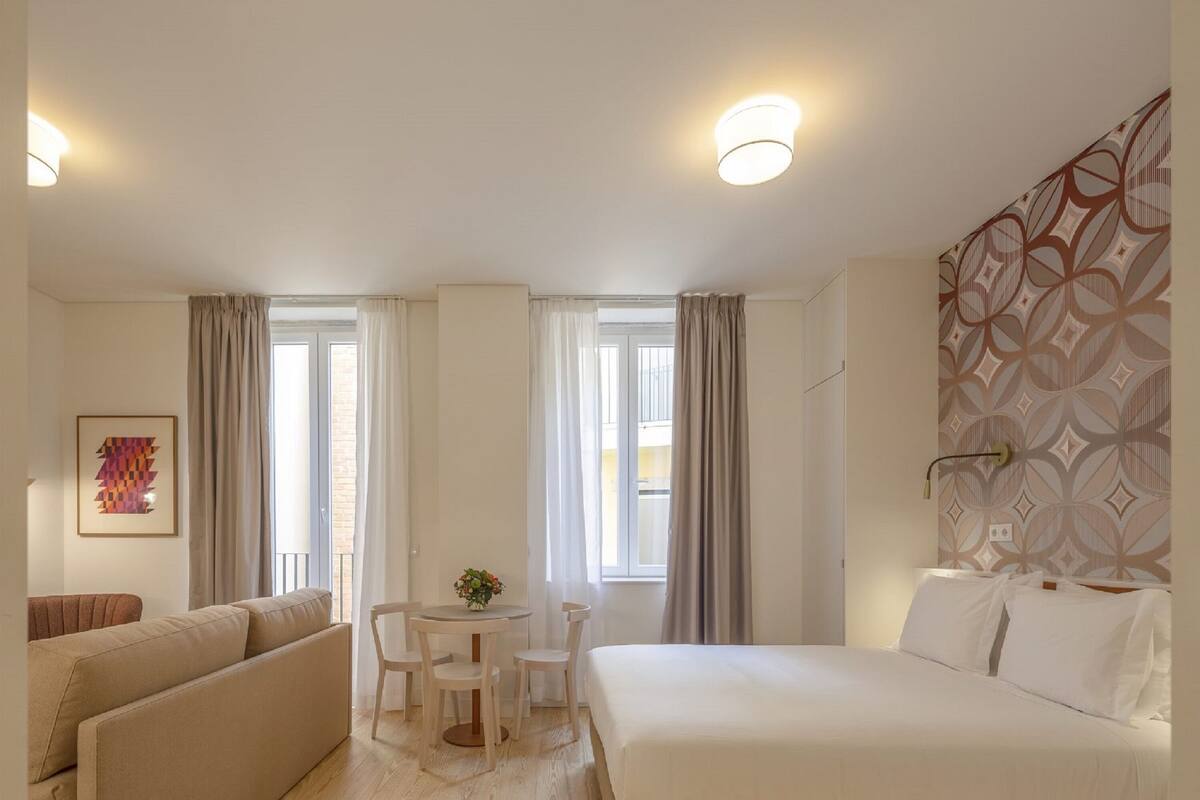 A hotel room with a bed, a sofa, a small table with chairs, and a window with curtains.