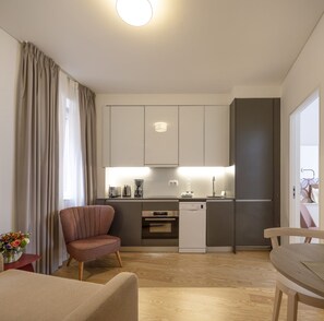 A modern kitchen with built-in appliances, a dining area with a table and chairs, and a living area with a sofa and a decorative vase.
