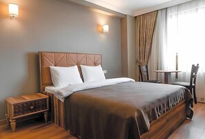 A hotel room with a large bed, bedside tables, a small table, and a chair. - Madame Roza (Istanbul)