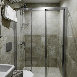 A glass-enclosed shower stall with a handheld showerhead, a towel rack, and a control panel on the wall. - Madame Roza (Istanbul)