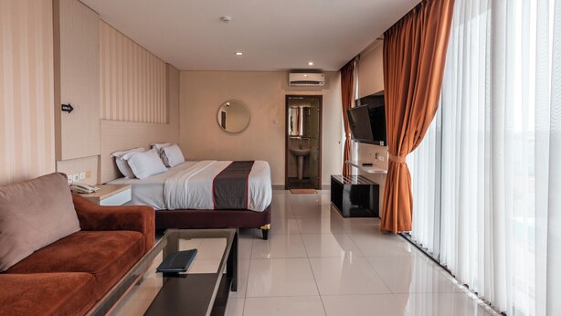 A hotel room with a bed, a sofa, a TV, and a bathroom visible through an open door. - Collection O Hotel Igloo (Cikarang)