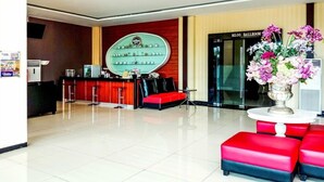 A hotel lobby with a reception desk, a red and black sofa, a round table with a vase of flowers, and a wall-mounted display of glasses and bottles. - Collection O Hotel Igloo (Cikarang)