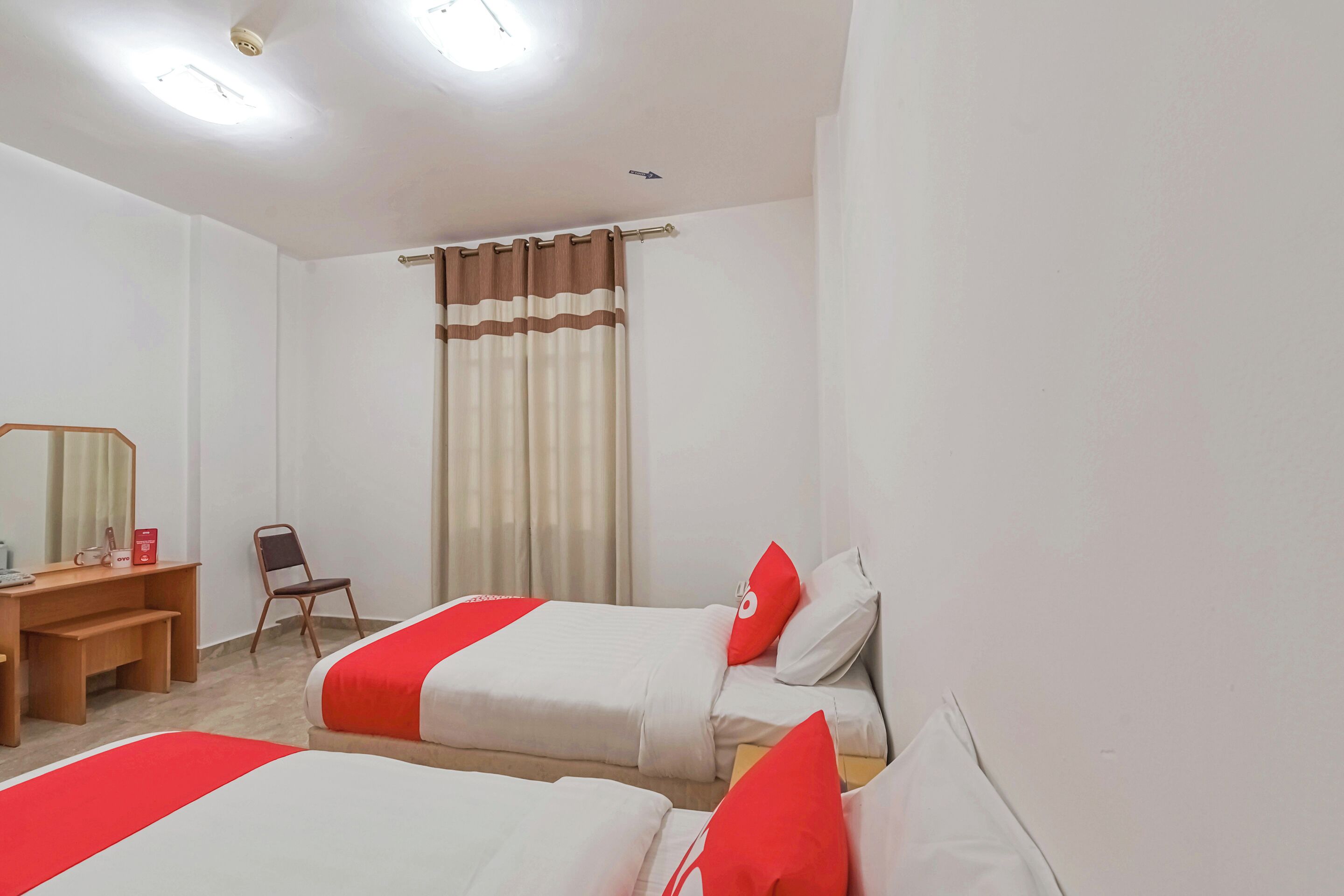 Habitación de hotel con dos camas, un escritorio, una silla y una ventana con cortinas.