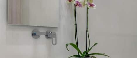 Casa de banho com lavatório branco, espelho e duas orquídeas em vasos.