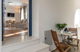 Una sala moderna con un sofá, una mesa de comedor con sillas, un televisor montado en la pared y una escalera que sube a otro nivel.