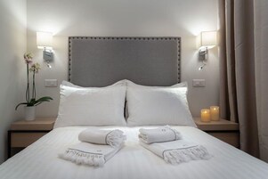 Una habitación de hotel con una cama grande, dos lámparas de noche, una planta en maceta y dos velas sobre la mesita de noche.