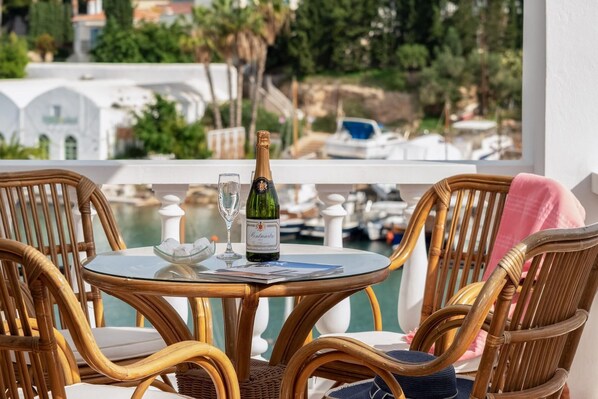 A table with a bottle of champagne, a glass, and a bowl of ice on a balcony overlooking a marina with boats and greenery. - Porto Vecchio Luxury Suites (Spetses)