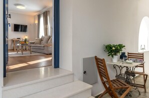 Ett modernt vardagsrum med en soffa, ett matbord med stolar, en tv som är monterad på väggen och en trappa som leder till ett annat våningsplan.