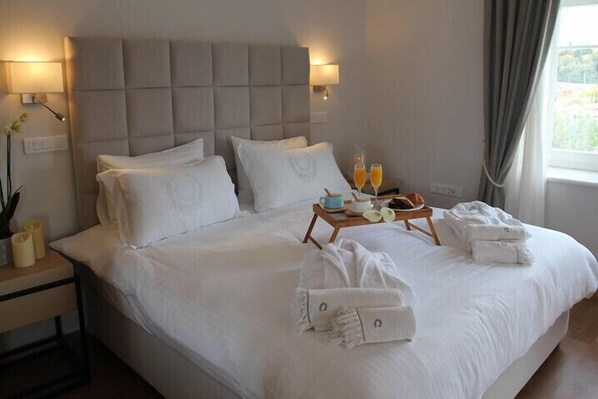 A neatly made bed with pillows, a bedside table with a lamp, and a tray with breakfast items. - Porto Vecchio Luxury Suites (Spetses)