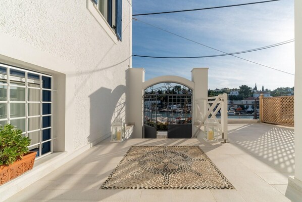 Una entrada protegida con vista a un puerto deportivo, un edificio blanco con una ventana y una alfombra estampada en el suelo.