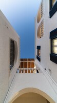 Un estrecho callejón con una escalera de madera que conduce a un nivel superior, flanqueado por edificios con paredes blancas y contraventanas azules.