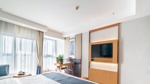 Et moderne hotelværelse med en stor seng, et skrivebord, en stol, et fjernsyn og et vindue med gardiner.