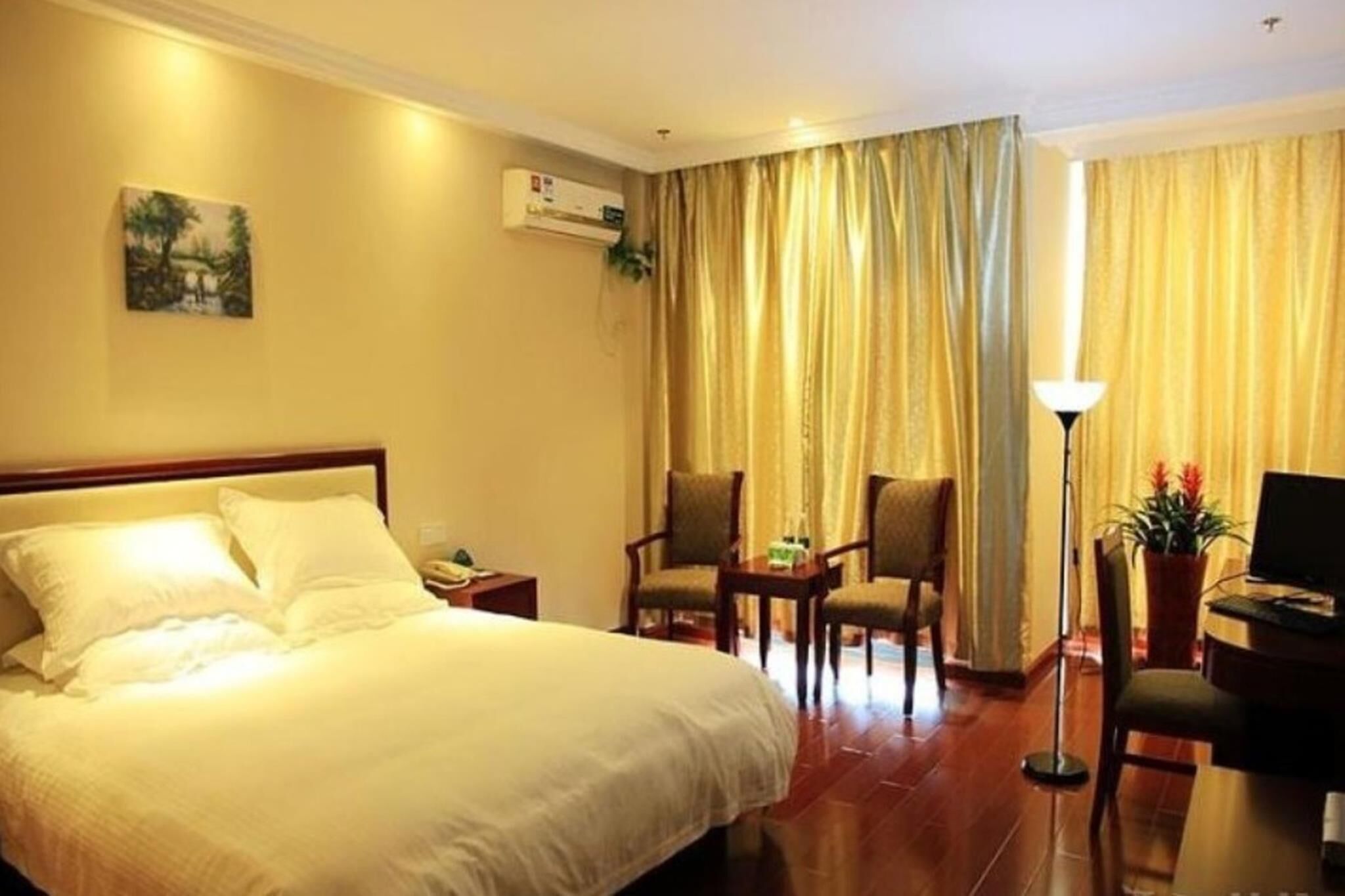 Habitación de hotel con una cama grande, dos sillones, un escritorio con una computadora y una ventana con cortinas.