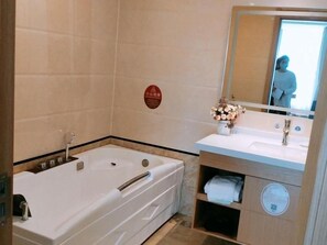 A modern bathroom with a large bathtub, a vanity with a mirror, and a small shelf with towels. - Greentree Inn Jiangsu Wuxi Hudai Fuan Commercial Plaza Business Hotel (Wuxi)
