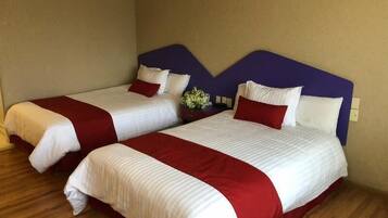 Dos camas individuales con ropa de cama blanca y roja, un cabecero morado y piso de madera.