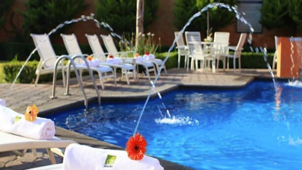 A swimming pool with lounge chairs and a table, surrounded by greenery.