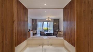 A modern bathroom with a large bathtub, wooden paneling, and a view of a dining area with a table and chairs.