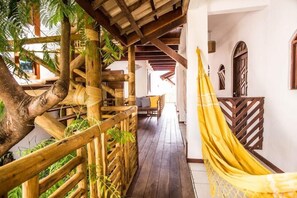 Una escalera de madera con una hamaca, rodeada de follaje y una barandilla de madera.