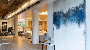 A spacious hotel lobby with a modern design, featuring a large abstract painting, a reception desk, and comfortable seating areas. - Mikelina Hotel (Pallini)