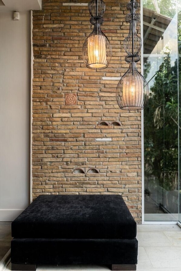 A modern room with a brick wall, a black cushioned bench, and two hanging pendant lights. - Mikelina Hotel (Pallini)