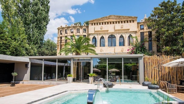 A modern pool area with a clear pool, lounge chairs, and a building with arched windows in the background. - Mikelina Hotel (Pallini)