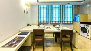 Uma cozinha moderna com máquina de lavar, sala de jantar com cadeiras e uma mesa posta para dois.