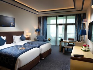 Hotellihuone, jossa on suuri sänky, työpöytä, tuoli, televisio ja parveke, jossa on verhot.