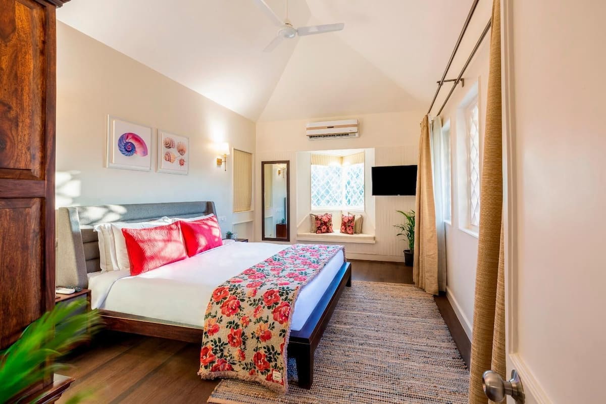 Une chambre avec un lit, un ventilateur de plafond, un appareil de climatisation, une fenêtre avec des rideaux et un téléviseur fixé au mur.