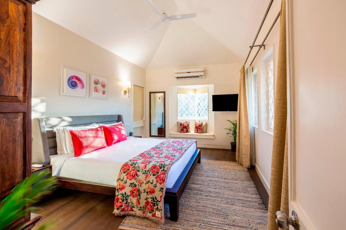 A bedroom with a bed, a ceiling fan, an air conditioning unit, a window with curtains, and a wall-mounted TV.