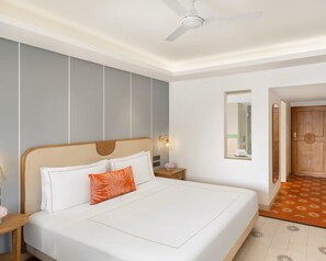A hotel room with a bed, a nightstand, a wall-mounted mirror, and a door leading to another room. - amã Stays & Trails, Beach Madh Island Mumbai (Mumbai)