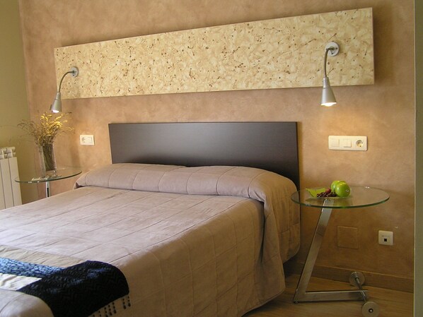 A bedroom with a bed, a nightstand, a wall-mounted light, and a small table with a vase and fruit. - Aqua Luna Spa (Cimanes del Tejar)