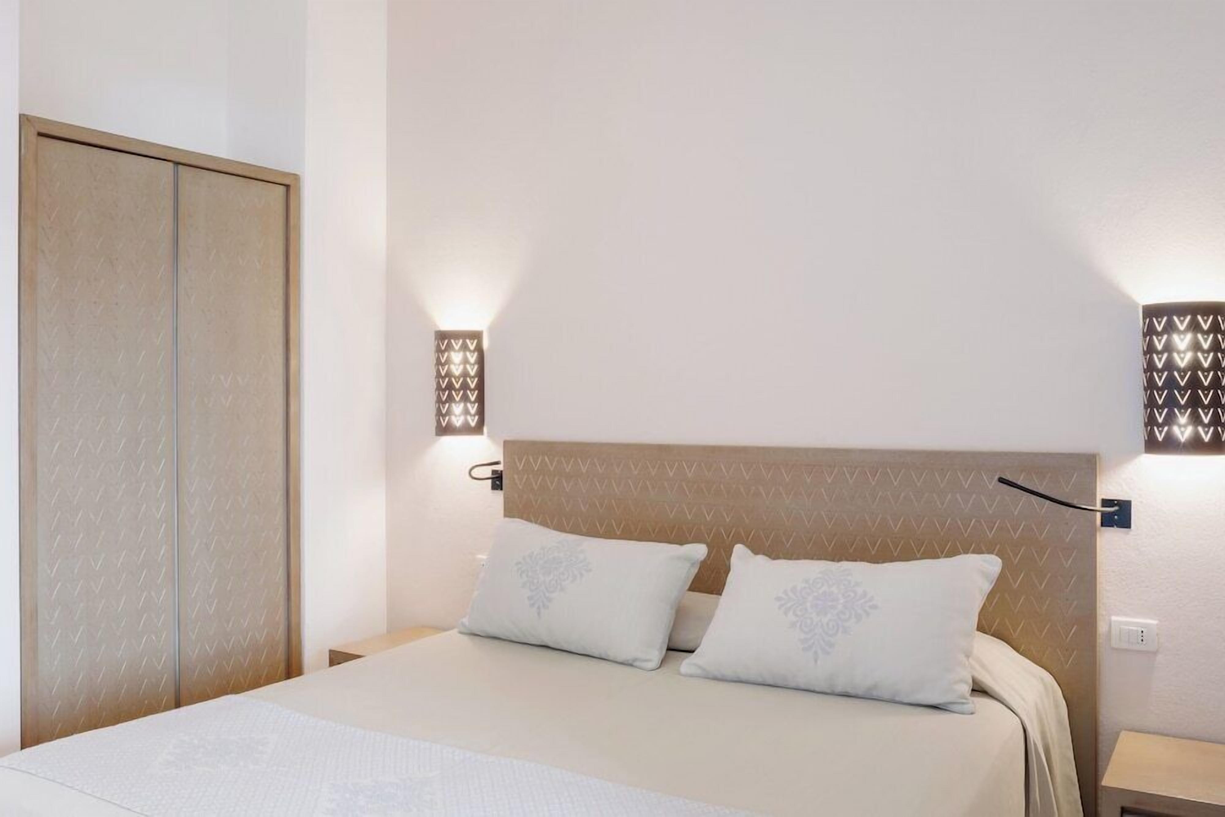 Una habitación de hotel con cama, lámparas de noche y un armario.
