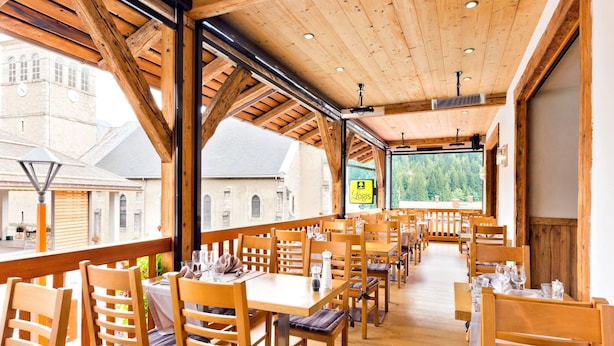 A restaurant with wooden interiors and large windows offering views of buildings and trees.