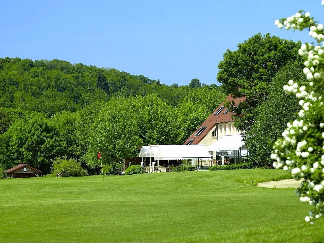 A golf course with a clubhouse, surrounded by lush greenery and trees.