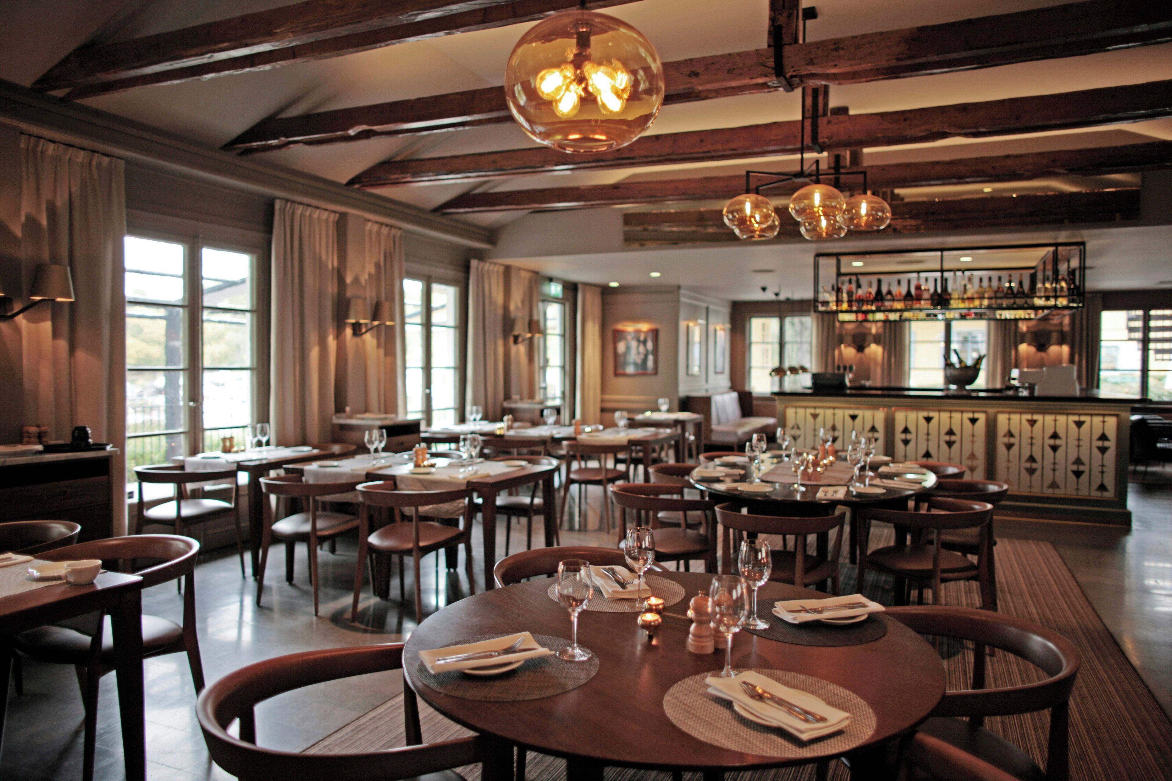 En restaurang med flera bord, stolar och en bardisk med hyllor fulla av flaskor.