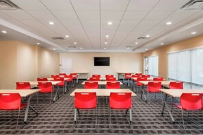 Uma sala de conferências com várias mesas e cadeiras, uma TV de tela plana na parede e uma grande janela em um dos lados.