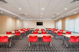 A conference room with multiple tables and chairs, a flat-screen TV mounted on the wall, and a large window on one side.