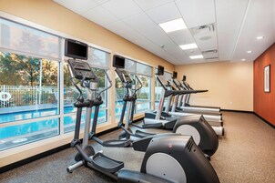 A gym with treadmills and exercise bikes, large windows, and a view of a swimming pool.